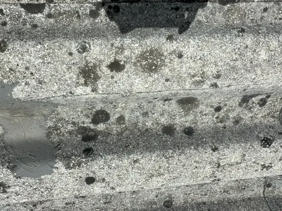 Corrugated fibre-cement roof sheet eroded back to the fibres, pitted, covered in lichen and cracked