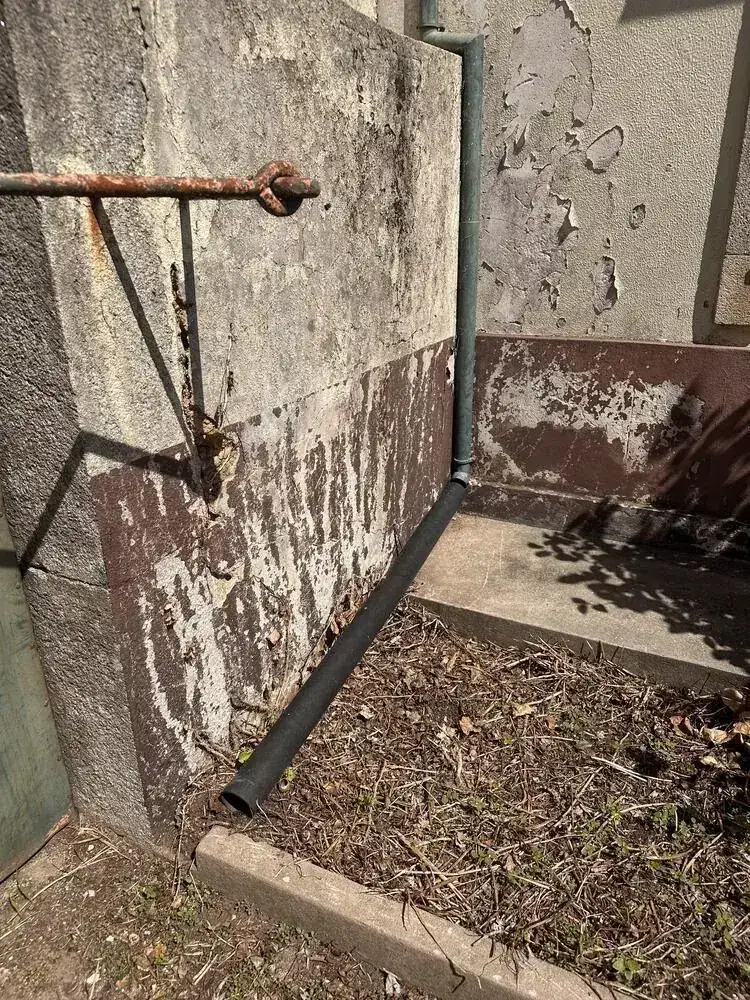 A downpipe discharging rainwater straight against the base of a wall