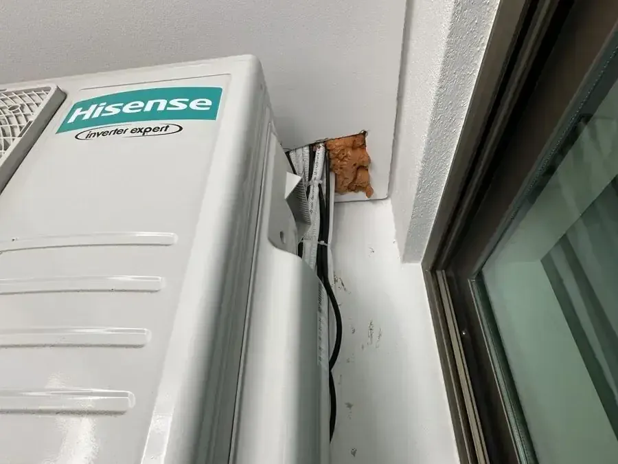Air-conditioning pipework through a wall packed with bare expanding foam and rust streaks below