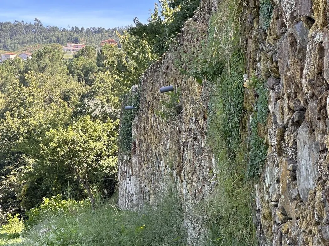 Paved path along the street side of a granite house with no drainage between the lane and the wall