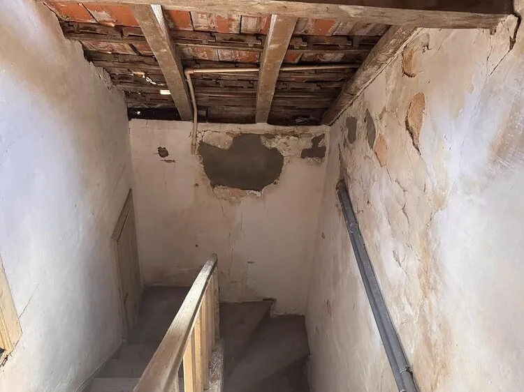 Teto aberto e vigas de madeira à vista sobre a escada de uma casa antiga