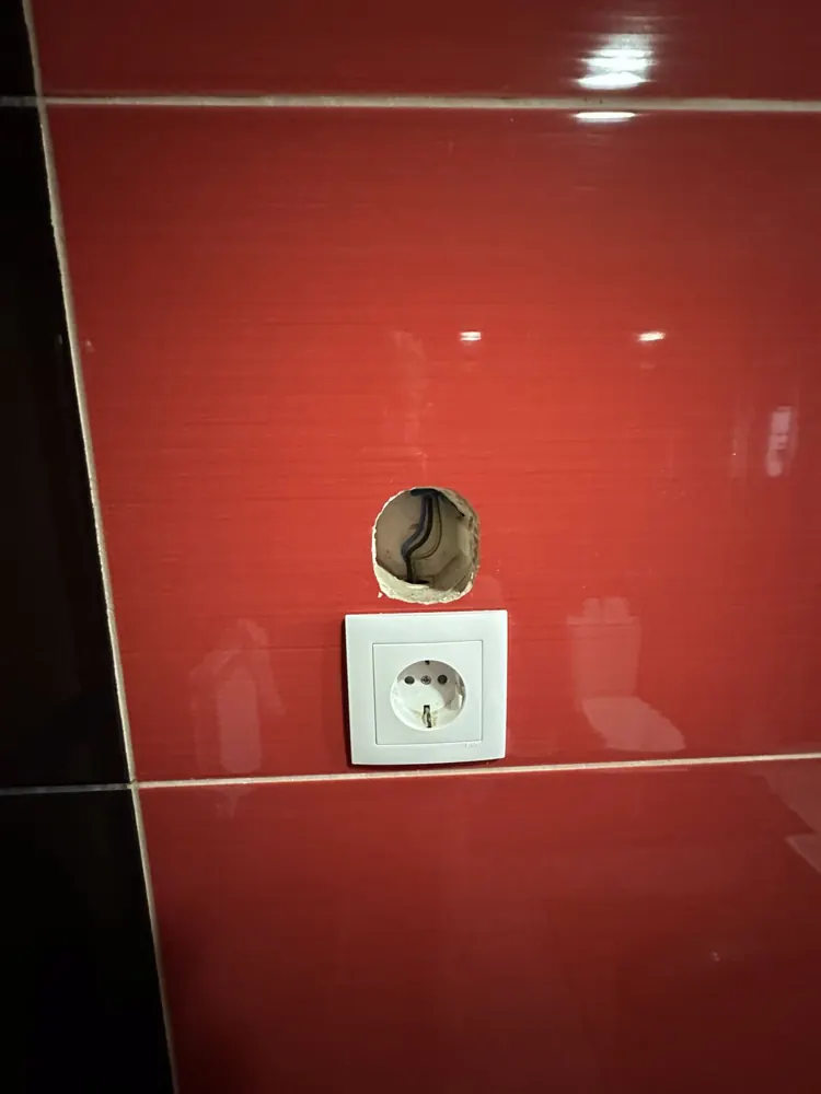 Socket next to a rough hole cut through a glazed wall tile