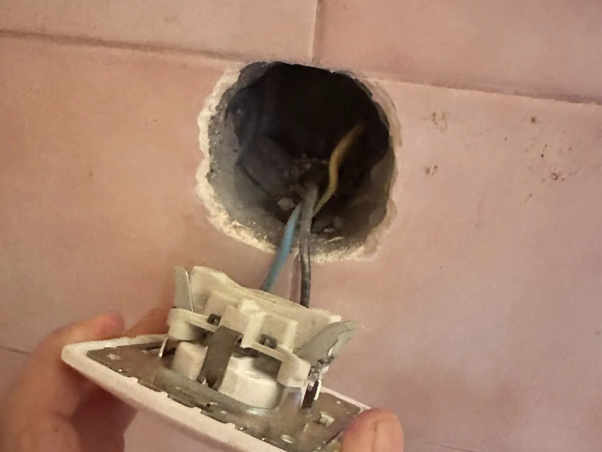 Wall socket pulled out of a broken tile with the wiring exposed
