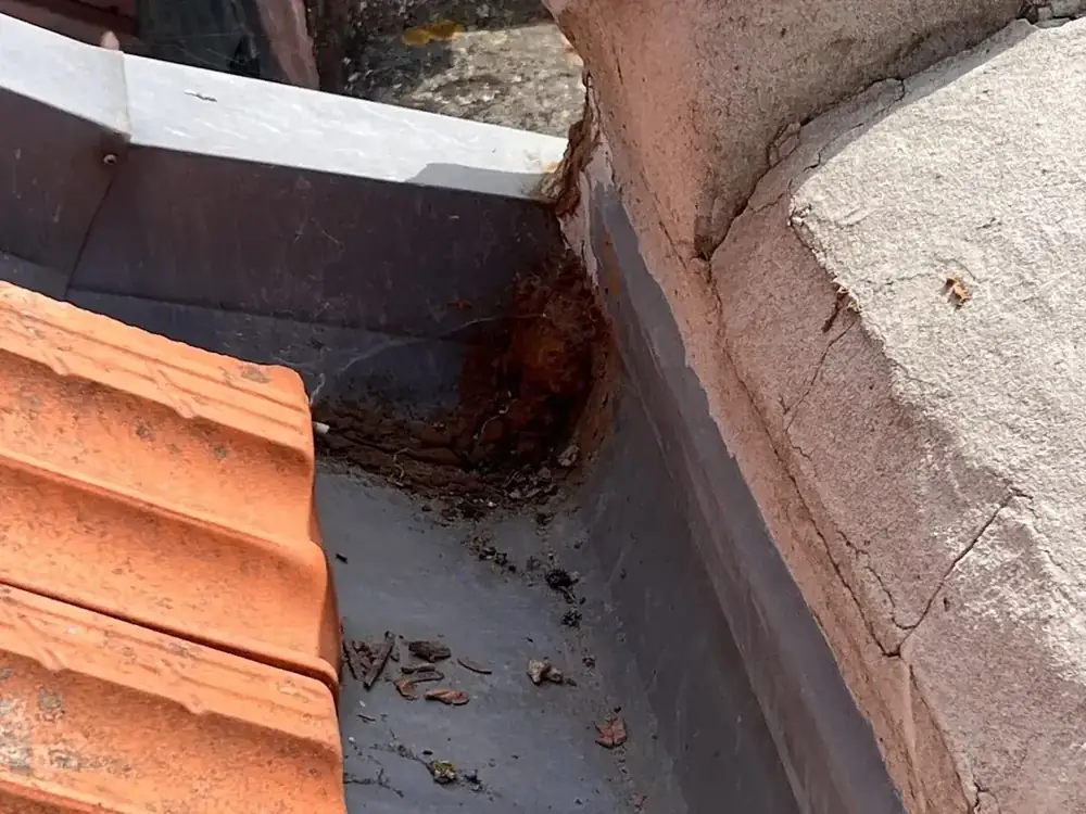 Telhado de telha a encontrar uma platibanda, com manchas de ferrugem na caleira